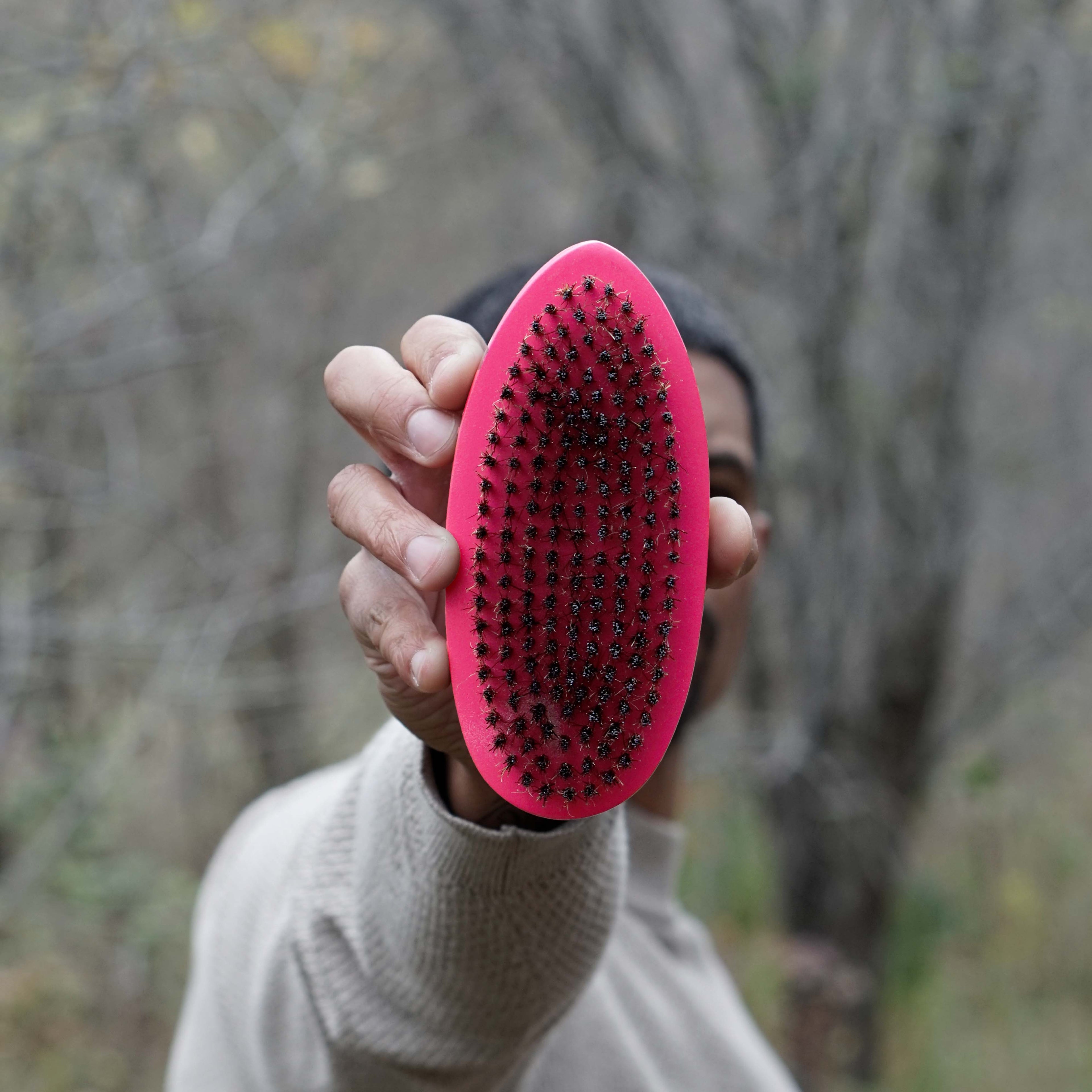Person holding a pink hard wave brush with a blurred natural background