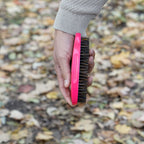 Hand holding a pink brush with bristles against a blurred natural background