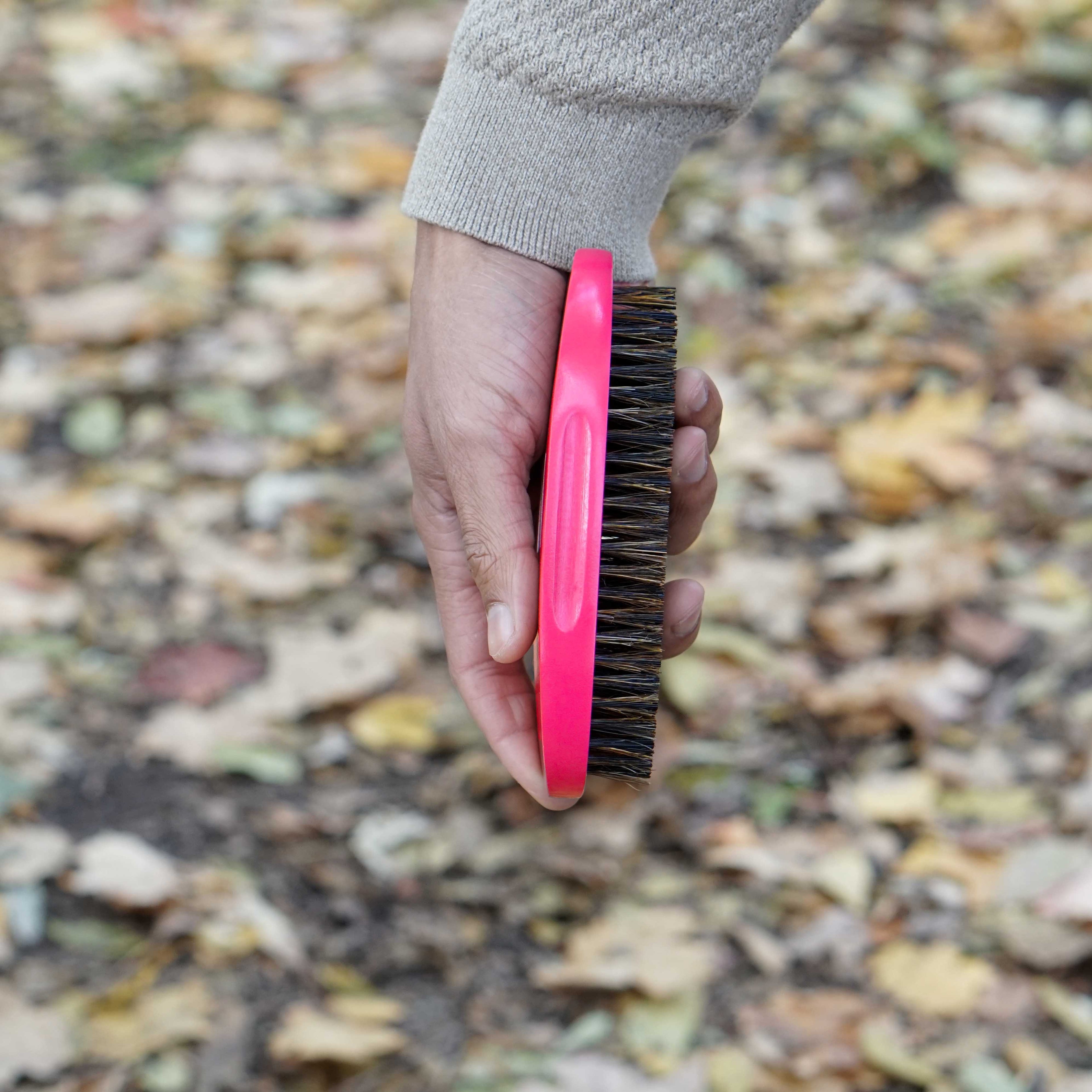 Hand holding a pink brush with bristles against a blurred natural background